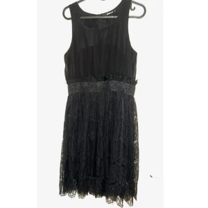 Svart spetsklänning med glittermidja-Gina Tricot - Supersnygg svart kortklänning med ärmlös design och markerad midja med glittrigt band. Kjolen är i vacker spets med fina detaljer och lätt transparent känsla. Perfekt för dig som vill sticka ut med en elegant och trendig look.