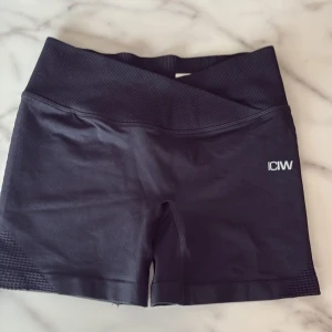 Svarta träningstights shorts från ICANIWILL - Svarta shorts från ICANIWILL med hög midja och omlott-detalj i midjan. Tillverkade i stretchigt material, perfekta för träning. Diskret logga framtill och ribbad linning för extra komfort.