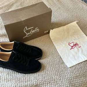 Svarta sneakers från Christian Louboutin - Snygga svarta sneakers från Christian Louboutin i mocka med klassisk röd sula och svarta skosnören. Skorna har rund tå och platt sula, samt exklusiv känsla med läderfoder. Perfekta för dig som vill sticka ut med stilrena detaljer.