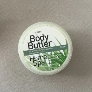 Gunry Body Butter Aloe Vera & Kamomill - Body butter från Gunry med aloe vera och kamomill, 250g. Ger en fräsch, mjuk och återfuktad känsla på huden. Perfekt för torr och känslig hud, doftar fräscht och har en krämig konsistens. Kommer i en rund plastburk med vit och grön design.