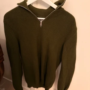 Olivgrön stickad half zip-tröja Zara - Säljer en olivgrön stickad tröja från Zara med half zip-dragkedja och hög krage. Tröjan har långärmad passform och är ribbstickad för en snygg struktur. Perfekt för lager-på-lager under hösten och vintern.