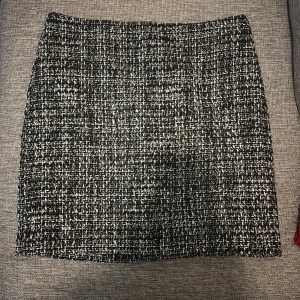 Svartvit rutig kjol från Åhléns - Snygg svartvit kortkjol från Åhléns i rutigt mönster. Kjolen har en rak passform och är tillverkad i ett grovt, strukturerat tyg som ger en cool och trendig look. Perfekt att styla med boots eller sneakers för en modern vibe.