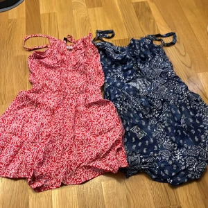 2 mönstrade sommarshorts med smock - Två par shorts med smock i midjan och tunna axelband. Ena paret är rödvitt med blommigt mönster, det andra är marinblått med paisley och vita detaljer. Båda är luftiga och perfekta för varma dagar. Materialet känns som tunn bomull eller viskos.