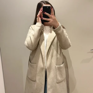 Beige kappa från VILA med bälte - Snygg beige kappa från VILA i klassisk modell med stora fickor och bälte i midjan. Kappan har en rak passform, perfekt för höst och vinter. Enkel att styla och fin till alla outfits. (Finns några fläckar då den e ganska använd)