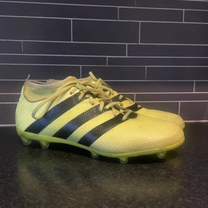 Gula Adidas fotbollsskor - Snygga fotbollsskor från Adidas i en fräsch gul färg med klassiska svarta ränder på sidorna. Skorna har snörning och mönstrad sula med dobbar för bra grepp på planen. Använda väldigt sparsamt och inga som helst defekter! Storlek 43-1/3. Tveka inte att höra av dig🤩 Pris kan diskuteras vid snabb affär✅