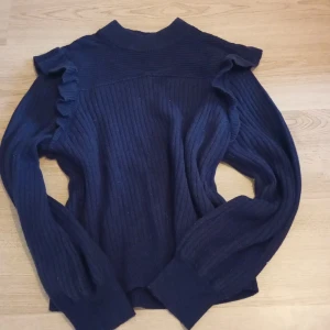 Mörkblå stickad tröja & Other Stories - Supersnygg mörkblå stickad tröja från & Other Stories Paris Atelier. Tröjan har ribbad struktur, volangdetaljer längs axlarna och långa ärmar. Perfekt för dig som gillar en trendig och bekväm look med det lilla extra.