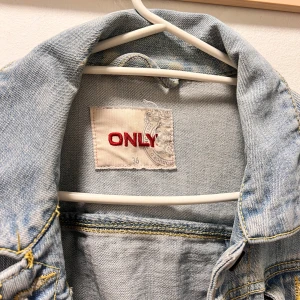Ljusblå jeansjacka från ONLY, stl 36 - Snygg ljusblå jeansjacka från ONLY med klassisk krage, knappar framtill och coola sömdetaljer på bröstfickorna. Jackan har långa ärmar och är perfekt att slänga över en hoodie eller t-shirt för en chill look.
