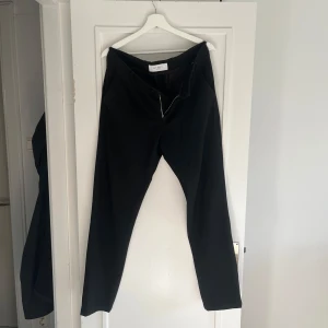 Svarta byxor från Les Deux - Snygga svarta kostymbyxor från Les Deux med klassisk rak passform. Byxorna har bälteshällor, sidofickor och bakfickor. Perfekta för en clean look.