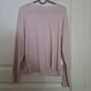 Ljusrosa stickad tröja - Mysig ljusrosa stickad tröja med lång ärm och rund hals. Tröjan har en avslappnad passform och små slitsar i sidorna, vilket ger en cool och enkel look. Perfekt att matcha med jeans eller kjol för en chill stil.