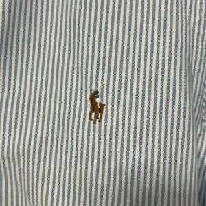 Ralph Lauren Oxford Skjorta - Klassiska Oxford skjortan från Ralph Lauren i den ikoniska blå-randiga färgen. Skjortan har den ikoniska multi-färgade broderade loggan på bröstet. Hör av er vid funderingar!