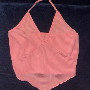 Rosa topp - Säljer en rosa ribbad linne-topp med halterneck och v-ringning. Toppen har en croppad passform med spetsig nederkant och tunna axelband. Perfekt för varma dagar eller när du vill ha en chill och trendig look.