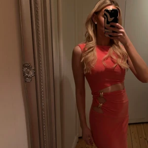 Korallfärgad långklänning med cut out ifrån ASOS! helt ny - Snygg långklänning i korall med cool cut out-detalj i midjan och guldfärgade spännen. Ärmlös modell med figurnära passform och rund halsringning. Bara provat, helt ny, prislapp kvar. Storlek S. Men passar mig som är en S/M🧡 slutsåld på hemsidan 