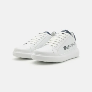 Valentino vita sneakers med logga - Snygga vita sneakers från Valentino med svart logga på sidan och mörkblå detaljer vid häl och plös. Skorna har rund tå, platt sula och klassisk snörning. Tillverkade i skinn för en lyxig känsla och stilren look.