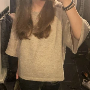 Beige stickad tröja med vida ärmar - Mysig beige stickad tröja med vida trekvartsärmar och avslappnad passform. Perfekt för lager-på-lager och passar till både jeans och kjol. Enkel och stilren design som är lätt att matcha med olika outfits.