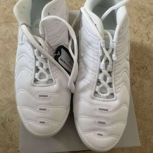 Nike Air Max Plus vita sneakers - Nike Air Max Plus i helvitt med ikoniska vågiga detaljer och synlig Air Max-dämpning i sulan. Ovandel i mesh och syntet, med vita snören och svart yttersula. Swoosh-logga på sidan och Tn Air-detalj under sulan. Riktigt clean och sportig look.