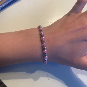 Rosa och silverfärgat pärlarmband - Snyggt armband med pärlor i rosa och silver, perfekt för att ge din outfit lite extra färg. Elastiskt band gör det enkelt att ta på och av. Pärlorna är runda och varvas i ett stilrent mönster. Passar dig som gillar en söt och trendig accessoar.