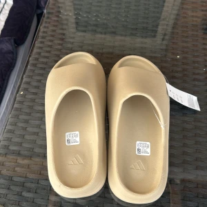 Adidas Yeezy Slide/pris kan diskuteras  - Adidas Yeezy Slide i beige med clean, minimalistisk design och bred rem över foten. Tillverkade i syntetmaterial med räfflad sula för extra grepp. Perfekta för chill dagar och enkel att matcha med streetwear.