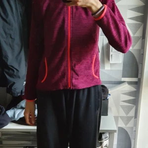 Vinröd fleecejacka med dragkedja - Snygg vinröd fleecejacka med hel dragkedja och kontrastfärgade detaljer vid fickor och ärmslut. Jackan har en sportig look och är perfekt för lager-på-lager. Långärmad och mjuk, passar dig som gillar bekväma och stilrena plagg.