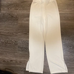 Vita ribbade byxor från Divided - Säljer ett par vita ribbade byxor från Divided by H&M. Byxorna har hög midja, raka ben och små slitsar nertill. De är gjorda i ett mjukt material som är riktigt skönt att ha på sig och extremt skönt under hösten eftersom de håller dig varma, jag har knappt använt dessa heller bara några enstaka gånger