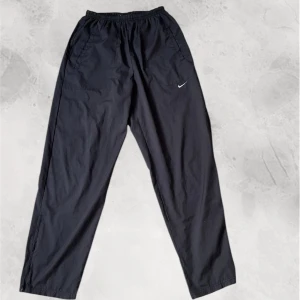 Nike trackpants - Säljer ett par svarta träningsbyxor från Nike med elastisk midja och sidofickor. Byxorna har en liten Nike-logga på ena benet och är perfekta för sport och träning. Inga defekter, helt nya. Kom privat för fler frågor!💫 Pris kan diskuteras