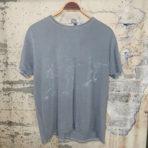 Grå t-shirt med skelett-tryck - Grå t-shirt i bomull med coolt tryck av skelett som åker skateboard över bröstet. Klassisk passform med korta ärmar och rund halsringning. Perfekt för dig som gillar streetstyle och unika prints.