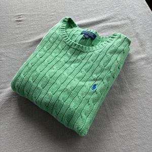 Grön kabelstickad tröja Polo Ralph Lauren - Snygg kabelstickad tröja från Polo Ralph Lauren i en fräsch grön färg. Klassisk rund halsringning och långärmad modell med blå broderad logga på bröstet. Perfekt för dig som gillar preppy stil och vill sticka ut lite extra. Står XL men känns mer som en M—————————————————— OBS‼️Jag är just nu ute på semester och kan inte packa ordrar på ungefär en vecka. Jag kan reservera varan åt er tills jag kommer tillbaka hem och packa den när jag  kommer hem. 