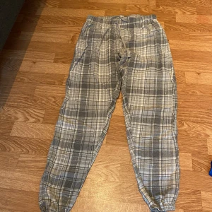 Grå-rutiga mjukisbyxor i bomull - Superbekväma grå mjukisbyxor med rutigt mönster och dragsko i midjan. Byxorna har elastiska benslut och är gjorda i mjukt bomullstyg, perfekta för chill dagar hemma. Snyggt avslappnad passform och klassisk look.