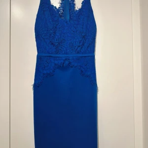 Spetsklänning  - Supersnygg kornblå klänning med spetsdetaljer upptill och smala axelband som korsas i ryggen. Klänningen har en figurnära passform och är ärmlös, med v-ringad hals och spets som ger en extra touch. Perfekt för dig som vill sticka ut!