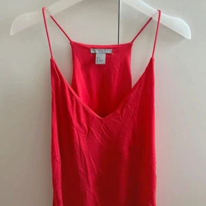 Röd ärmlös sommar topp med smala band - Enkel och snygg röd topp med smala axelband och v-ringning framtill. Linnet är ärmlös och har en rak, luftig passform som passar perfekt för varma dagar