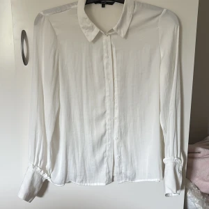 Vit skjorta från Vero Moda - Klassisk vit skjorta från Vero Moda i storlek S. Skjortan har lång ärm med fina detaljer vid mudden, knappar framtill och en stilren krage. Tillverkad i ett mjukt och lätt material som ger en snygg passform. Perfekt till jeans eller kostymbyxor. Köparen står för fraktkostnad:)