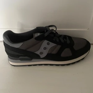 Saucony Shadow Originals HELT NYA! - Saucony Shadow Originals sneakers i olika nyanser av grått med svart och vit sula som är helt nya och sällsynta i detta pris. Ovandelen är i mesh och mocka med Sauconys ikoniska logga på sidan. Skorna har snörning och en klassisk retrostil som passar perfekt till streetwear.