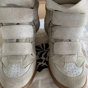 Beige wedge sneakers med kardborre - Chunky sneakers i beige mocka med coola paneler och flera breda kardborreband framtill. Skorna har en dold kilklack och vit perforerad tå, samt bruna gummisulor. Perfekta för dig som vill ha en sportig men edgy look.