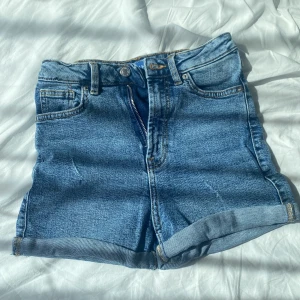 Blå jeansshorts  - Klassiska blå jeansshorts från Sinsay med hög midja och uppvikta benslut. Perfekta för varma dagar och enkel att matcha med allt. Aldrig använda av mig, fick dem begagnade. Katt finns i hemmet!!