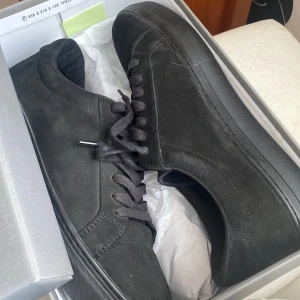 Svarta sneakers i mocka från Vagabond - Stilrena svarta sneakers från Vagabond i mjuk mocka med klassisk rund tå och platt sula. Skorna har svarta snören och diskreta sömmar för en clean look. Perfekta för dig som gillar minimalistisk stil och vill ha ett par schyssta vardagssneakers. Helt nya har bara provat dom inomhus skick 10/10