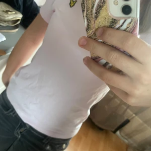 Ljusrosa t-shirt från Lyle & Scott - Säljer en ljusrosa t-shirt från Lyle & Scott med klassisk gul logga på bröstet. T-shirten är i mjuk bomull. Enkel och stilren modell som passar perfekt till jeans eller shorts.