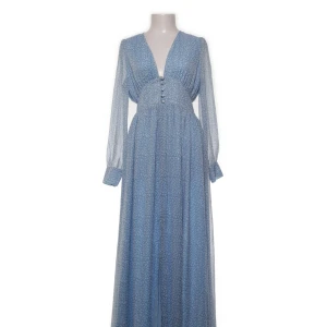 Adoore klänning - Långklänning i ljusblått med diskret mönster, djup v-ringning och knappar framtill. Klänningen har långa, transparenta ärmar med breda manschetter och en slits framtill. Perfekt för dig som vill ha en romantisk och flowy look.