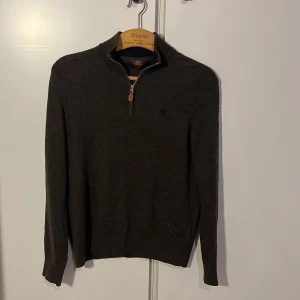 Mörkbrun merinoullströja Morris half zip - Snygg mörkbrun  tröja från Morris i 100% merinoull och i storlek XS. Tröjan har half zip med läderdetalj vid dragkedjan och en liten broderad logga på bröstet. Långärmad och med ribbade muddar för en clean look. Hör av er vid frågor.