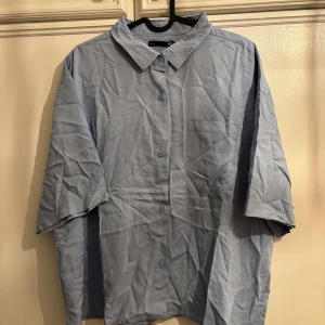 Ljusblå skjorta från 157, storlek XL - Ljusblå skjorta från 157 med korta ärmar och klassisk krage. Skjortan har knäppning framtill och en bröstficka. Tillverkad i mjuk bomull, perfekt för en chill och avslappnad stil. HELT NY