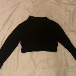 Svart croppad långärmad tröja - En svart, croppad långärmad tröja med enkel design och hög hals. Perfekt för dig som gillar en stilren och clean look. Tröjan är figurnära och passar till många olika outfits.