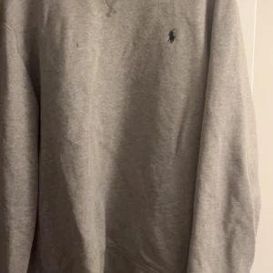 Grå sweatshirt från Polo Ralph Lauren - En klassisk grå sweatshirt från Polo Ralph Lauren med broderad logga på bröstet. Tröjan har rund halsringning och långa ärmar. Perfekt för en chill och stilren look. Tillverkad i mjuk bomullsmix som är skön att bära.
