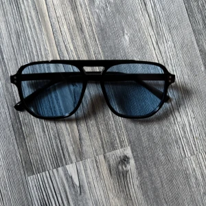 Svarta pilotbågar med blåtonade glas - Snygga svarta pilotglasögon med blåtonade glas och klassisk dubbelbrygga. Ramen är i plast och har en stilren, modern look som passar perfekt för dig som vill sticka ut lite extra. Helt nya