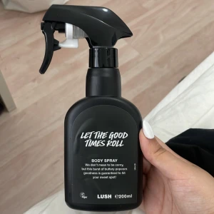 Lush Let The Good Times Roll Body Spray - En svart sprayflaska med lite mer än hälften i body spray från Lush, Let The Good Times Roll. Doften beskrivs som en söt och smörig popcornupplevelse. Flaskan har en modern, matt finish och tydlig vit text på framsidan. Vegansk och tillverkad i England.