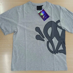 Grå t-shirt med svart graffiti-tryck - Snygg grå t-shirt med stort svart graffiti-inspirerat tryck som täcker både fram- och baksidan. Klassisk rund halsringning och korta ärmar. Tillverkad i mjuk bomull som känns skön mot huden. Perfekt för dig som gillar streetstyle och unika prints.