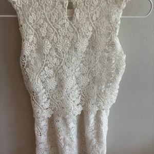 Vit spetsklänning med blommönster - Superfin vit kortklänning i spets med blommigt mönster. Ärmlös modell med rund halsringning och vackra detaljer i spetsen som ger en romantisk vibe. Perfekt för sommarens alla tillfällen!