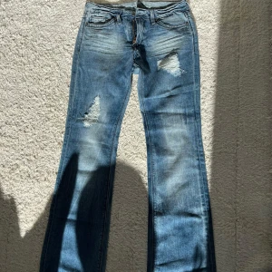 Blå bootcut jeans med slitningar - Snygga blå bootcut jeans med slitna detaljer och hål på låren. Jeansen har klassisk femficksdesign, skit snygga fickor. Köpta här på Plick men jag har aldrig använt dem, kunde inte ta bild på för dem passar inte mig.