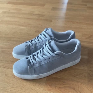 Grå mockasneakers från Selected Homme - Stilrena sneakers i ljusgrå mocka från Selected Homme. Klassisk modell med rund tå, platt vit sula och snörning. Perfekta för dig som gillar minimalistisk och clean stil. Skorna har en mjuk känsla och passar till det mesta.