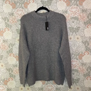 Grå stickad tröja från 157, storlek S oversized - Mysig grå stickad tröja från 157 i storlek S. Tröjan har en klassisk rund halsringning, ribbade muddar och lång ärm. Perfekt för lager-på-lager och chill dagar. Enkel och stilren design som funkar till det mesta.