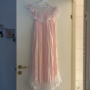 Ljusrosa spetsklänning från Komar - Romantisk långklänning i ljusrosa från Komar med vackra spetsdetaljer och volang vid axlar och nederkant. Klänningen har blommigt spetsmönster upptill och är ärmlös med en luftig, flowy passform. Perfekt för dig som älskar vintagevibbar och söta detaljer. Den är i storlek S/M!!!<3