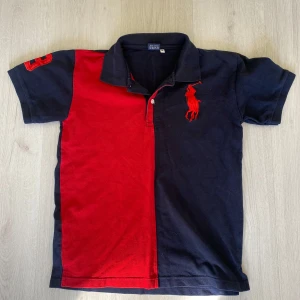 Ralph Lauren pikétröja röd/svart M - Snygg pikétröja från Ralph Lauren i storlek M. Tröjan är tvåfärgad med ena sidan röd och andra svart, har stor röd logga på bröstet och siffran 3 på ärmen. Klassisk krage och korta ärmar. Tillverkad i 100% bomull.