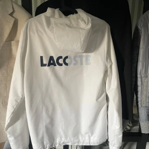 Lacoste tracksuit - Säljer nu min Lacoste Tracksuit/Dress som tyvärr ej kommer till användning, Riktigt snygg & unik nu till sommaren! ☀️både byxorna och vindjackan är Ny skick & har inga defekter. Hela dressen är köpt från Lacoste egna hemsida - ”Lacoste.com” & online kvitto finns ifall ni vill ha det med köpet. 🙌🏻Orginal priset ligger på 3000kr, men jag väljer att sälja billigare, PS Priset är EJ hugget i sten! 🪨🤩